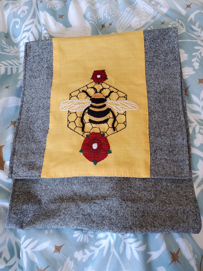 rectangular back made of grey wool with yellow linen front plate embroidered with a large bee and red roses