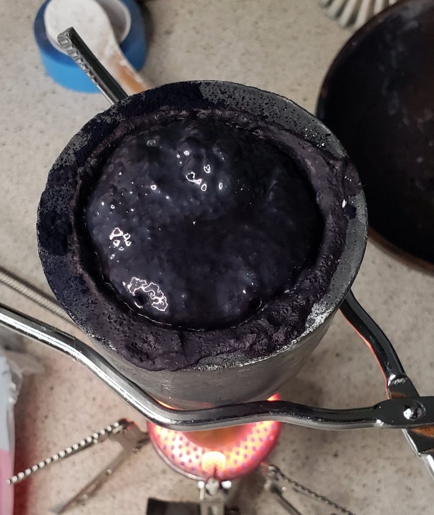 Small clay crucible over flame with slight bubbling indigo