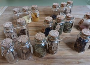 Small glass jars with cork lids containing a variety of dried herbs and spices