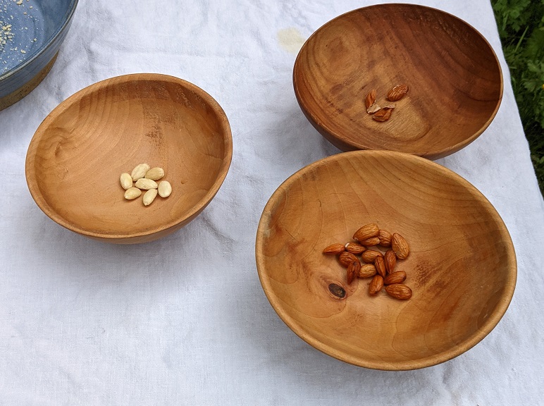 3 wooden bowls holding peeled almonds, almond peels, and soaked almonds