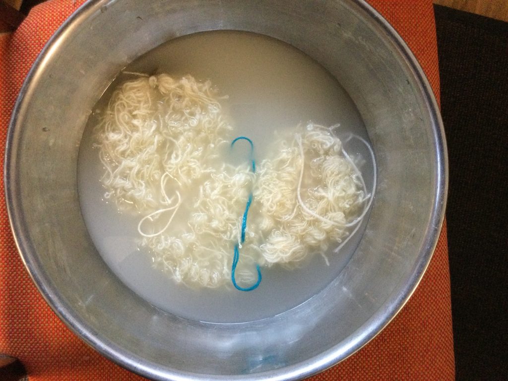 a white highly twisted skein yarn is in a steel bucket partially filled with cloudy water