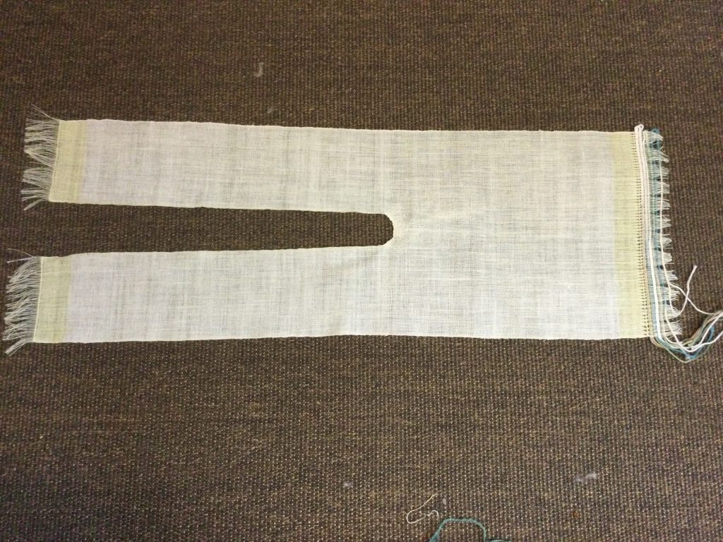 A woven piece of cloth that resembles a pant outline lays on an area rug.