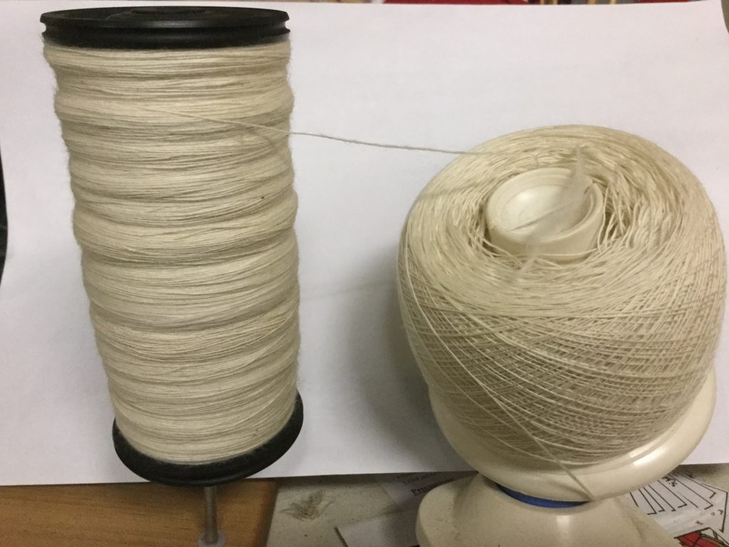 a large bobbin of finely spun wool sits beside a ball of another bobbin of finely spun wool