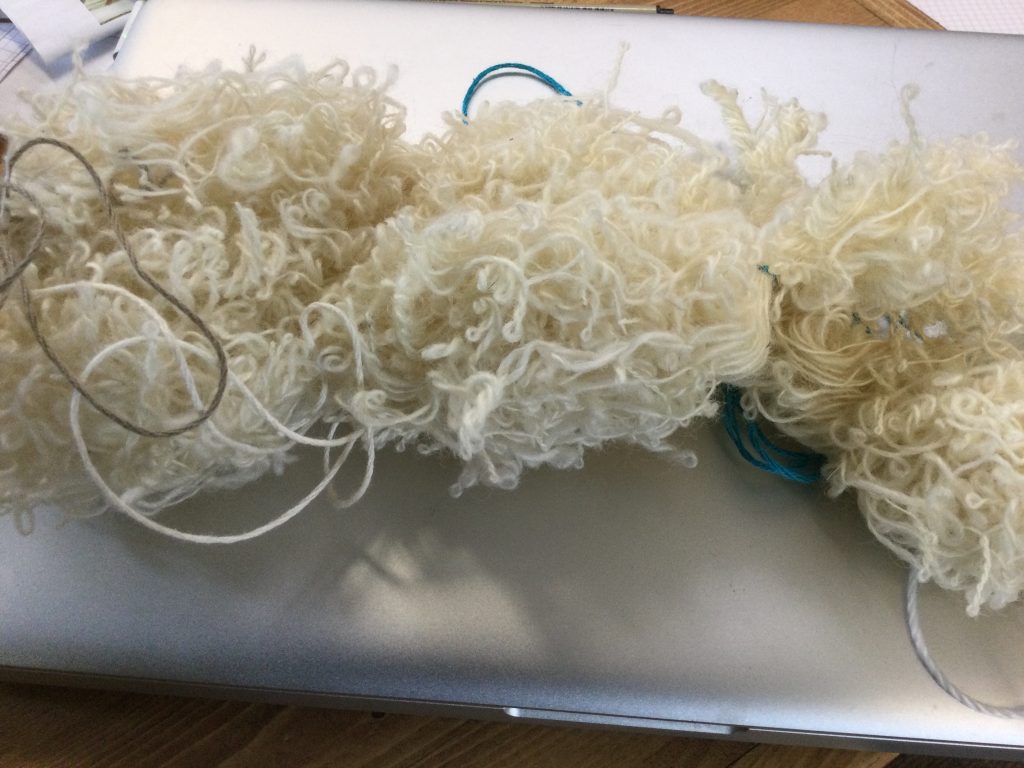 a highly twisted skein of white yarn, sits on top of a closed gray laptop