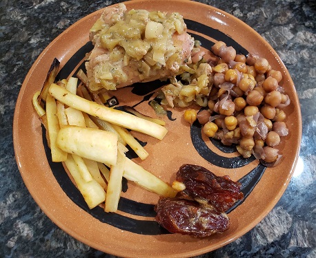A replica pottery dish containing fried parsnips, chickpeas, chicken in sauce, and candied dates served with pine nuts.