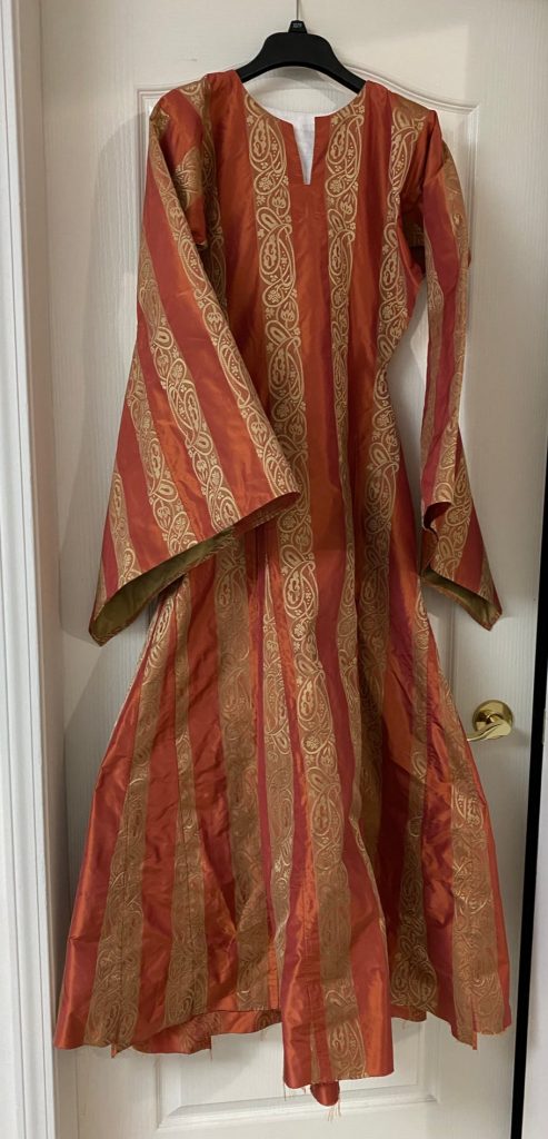 An orange dress with yellow brocade stripes hanging on a hanger with a white door as the background