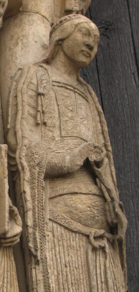 A stone statue of a twelfth century lady wearing a mantle closed with a cord
