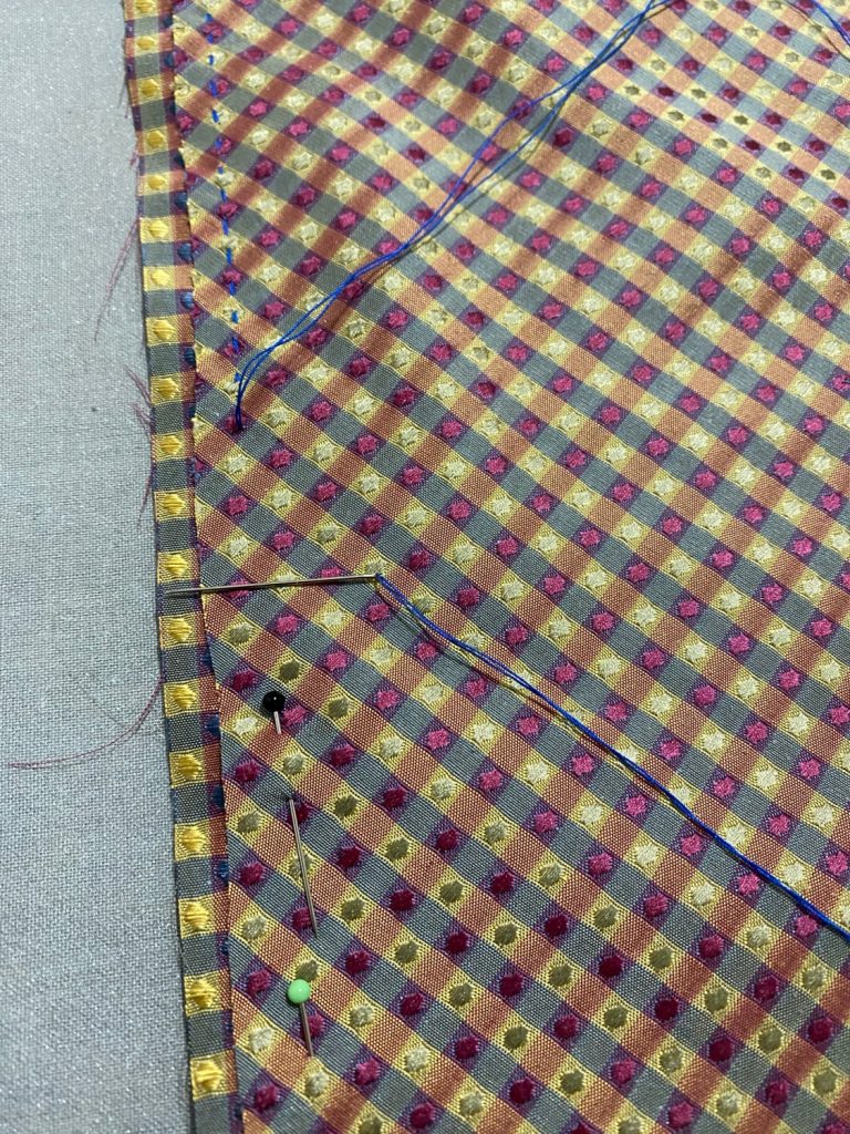 Two pieces of yellow, red and blue silk fabric offset from each other being sewed with blue thread