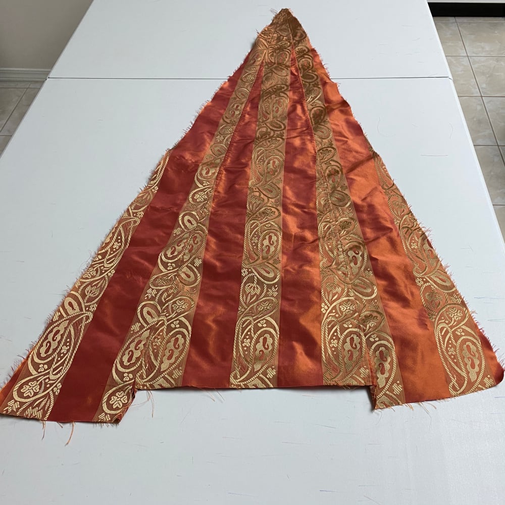 A triangle of orange fabric with yellow brocade stripes