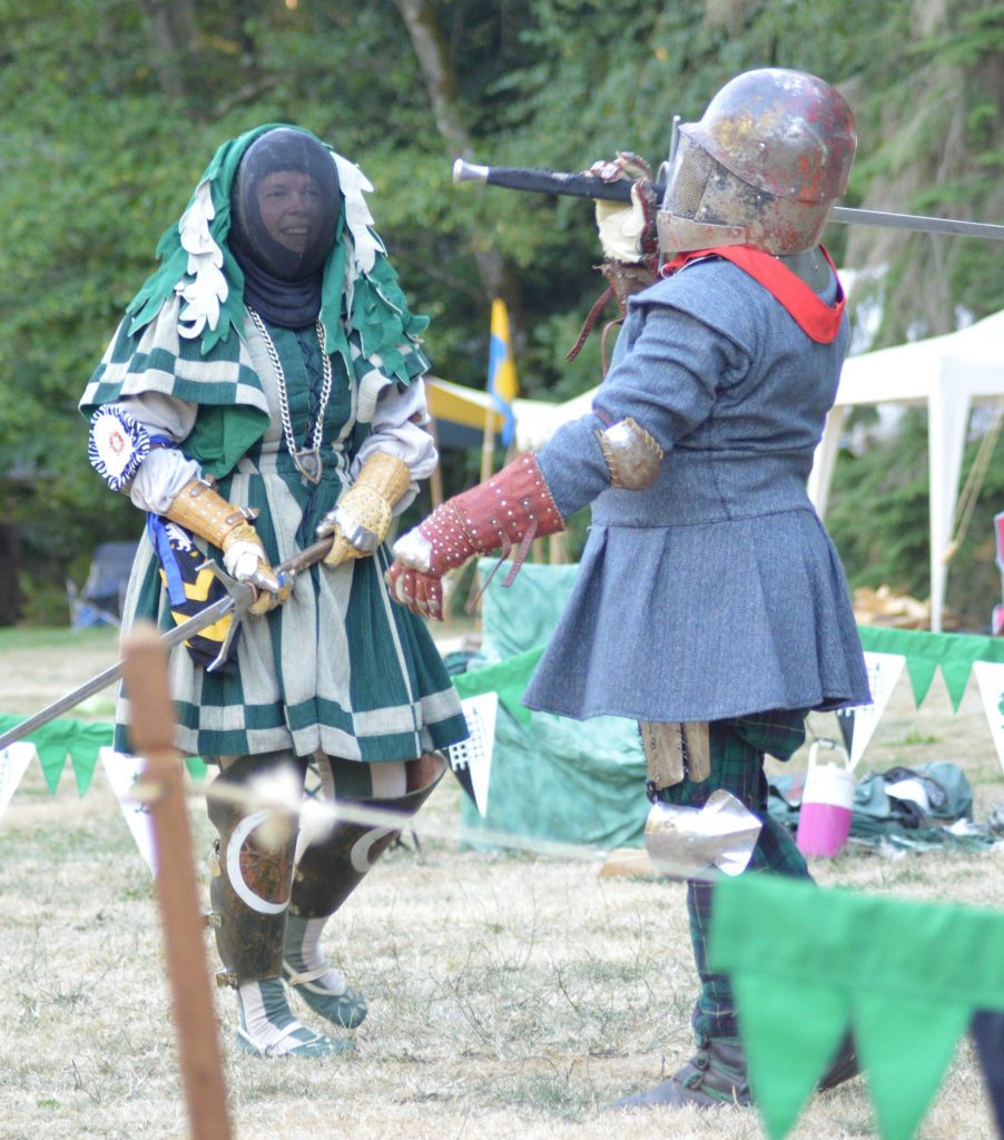 Woman in grey and green with a sword fighting man in blue with sword